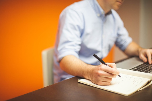 Article writers in Pakistan jotting down notes in a notebook at a desk with a laptop.